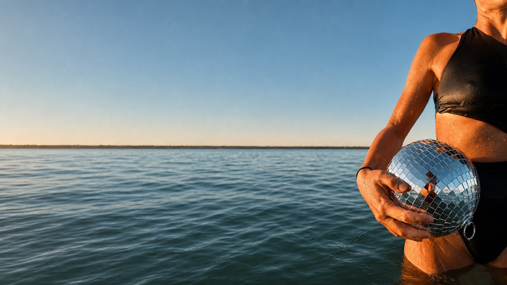 Nageuse tenant une boule à facettes dans la mer à l'heure dorée